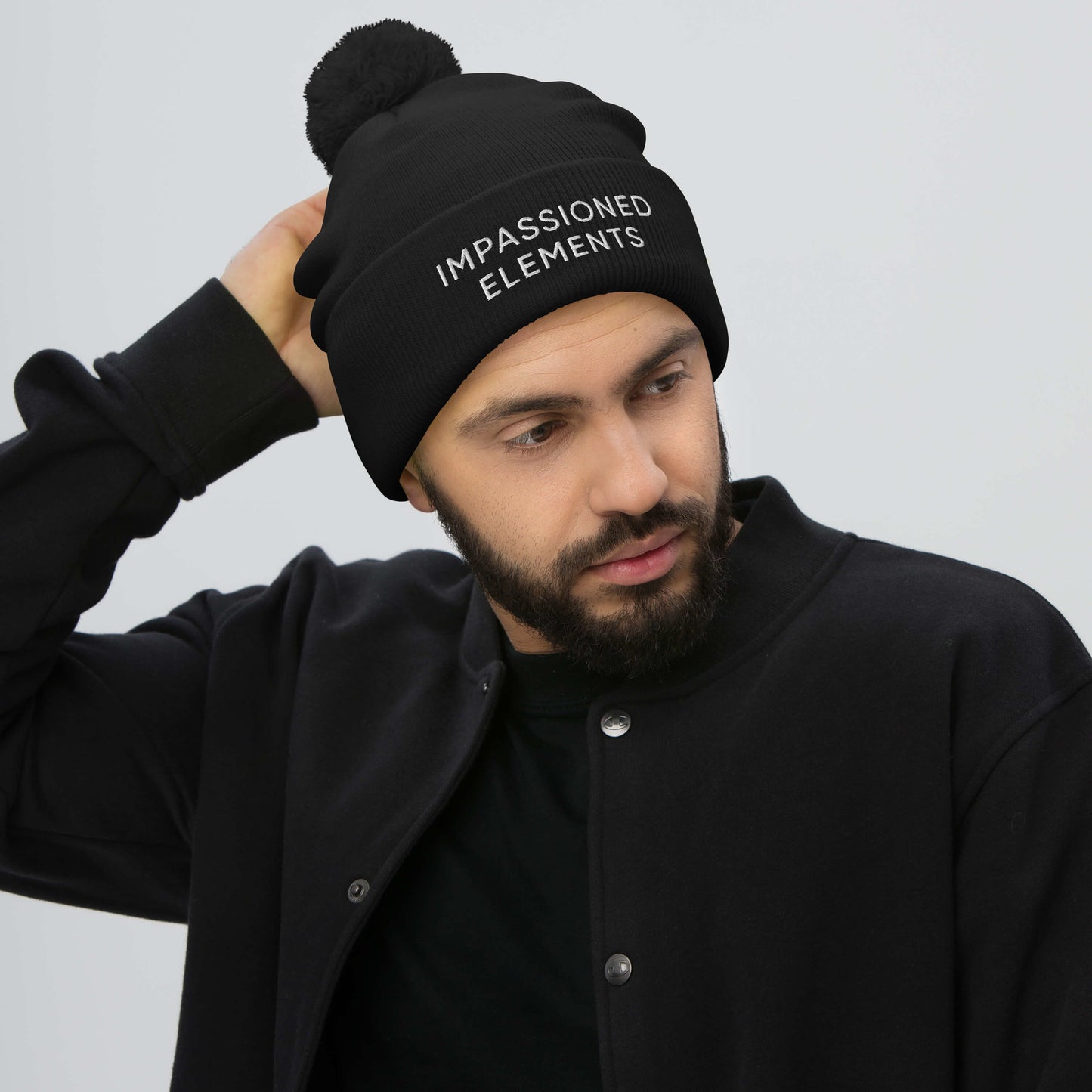 Male model wearing all black with stylish black pom-pom Impassioned Elements cuffed beanie to match