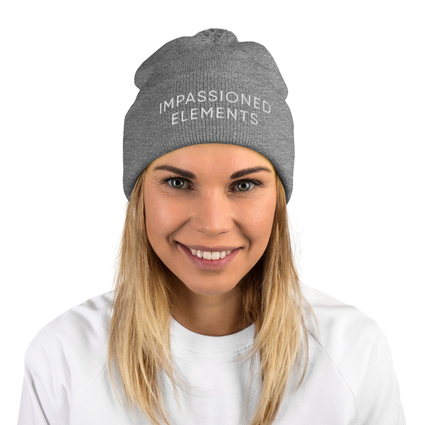 Cheerful woman showcasing a heather grey knitted pom-pom beanie hat with Impassioned Elements embroidery