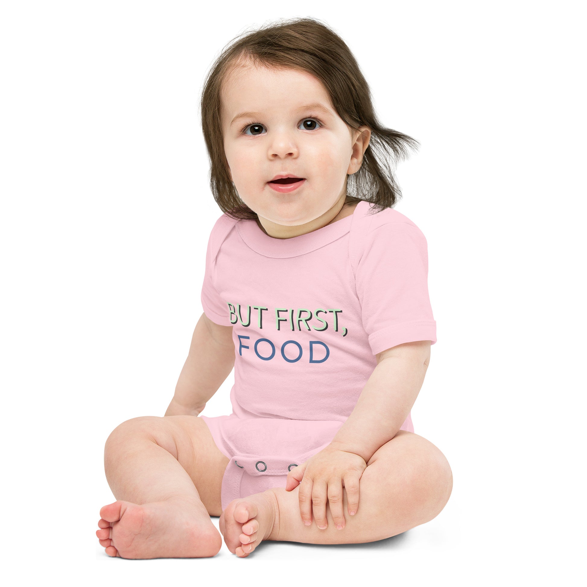 A delightful baby girl in a pink bodysuit with the words "but first food." Pure cuteness overload!