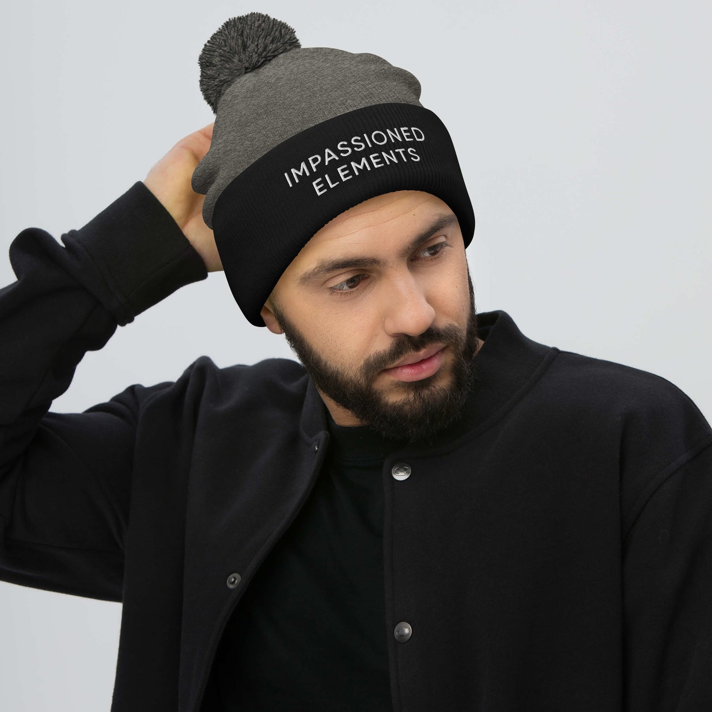 Cool and collected guy in a dark heather grey with black front cuffed pom-pom beanie adding a unique touch to his look