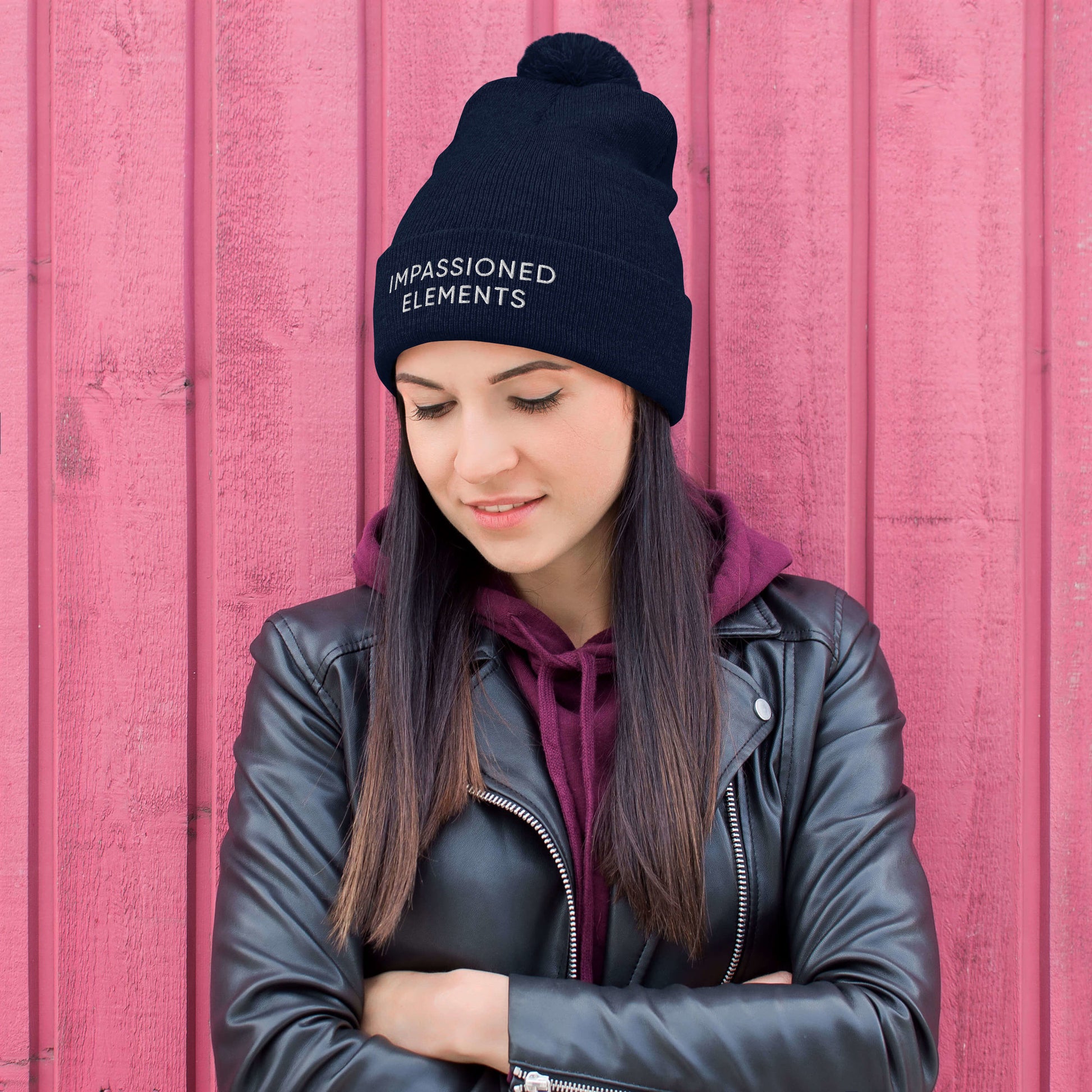 Smiling female model sporting a navy blue Impassioned Elements pom pom beanie