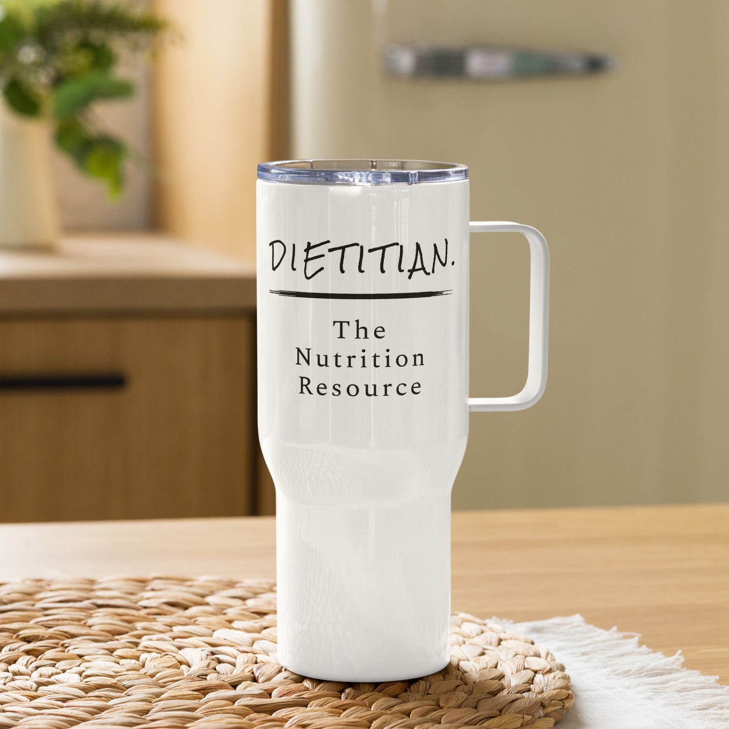 A white travel mug with the words "Dietitian. The Nutrition Resource" written on it displayed in the kitchen on a wicker place mat.